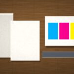 Stacks of unprinted paper and CMYK color blocks on a commercial print-shop production table, no people or text